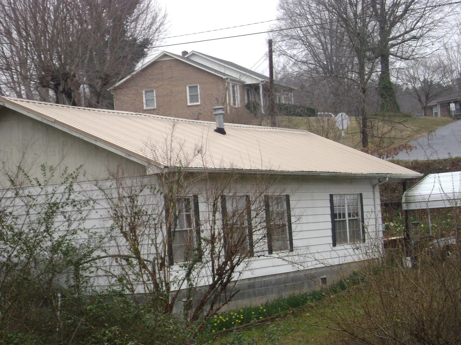 Tan metal roof on a white sided house set into a hillside — Commercial Roofing by Roofing Brothers in Woodland
