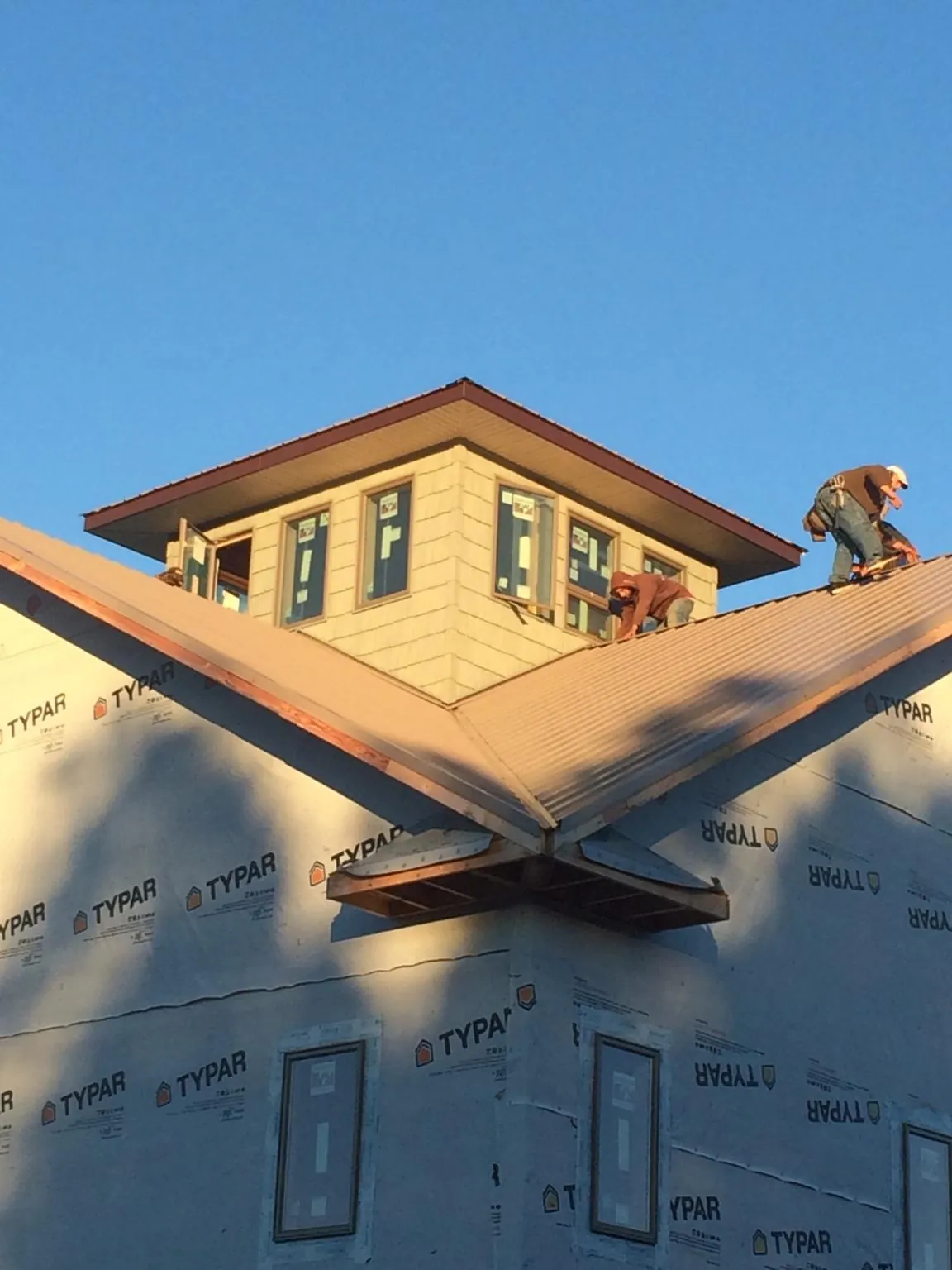 Roofers working around a rooftop cupola on a new metal roof at sunset in Woodland